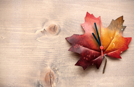 Autumn leaf with clock hands on top of a wooden backgroundの写真素材