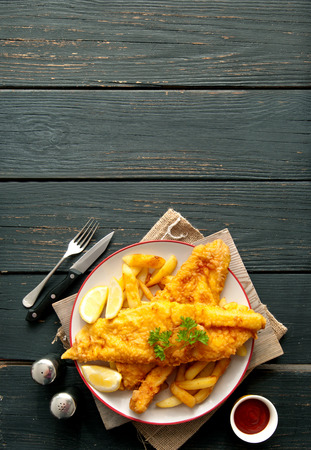Two pieces of battered fish on a plate with chipsの写真素材