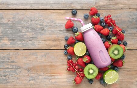Berry smoothie in a bottle with ingredients on top of a wooden background with spaceの写真素材