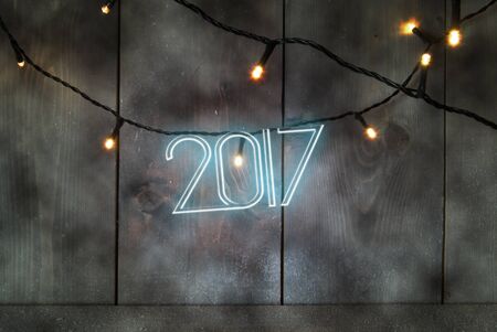 Neon text spelling 2017 on a wooden background with festive lightsの写真素材