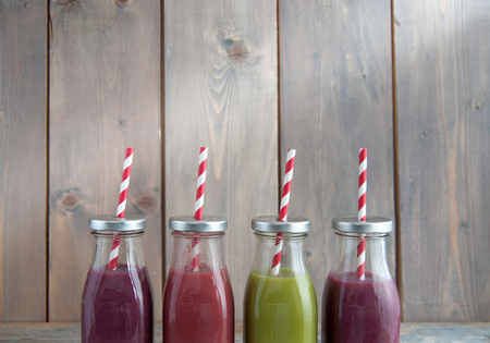 Flavoured smoothies in bottles over a wooden background with copyspaceの写真素材