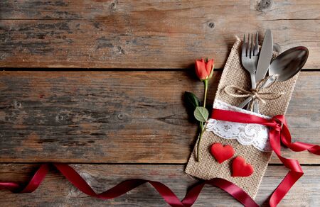Cutlery set inside pouch with hearts, red rose and silk ribbon over a wooden backgroundの写真素材