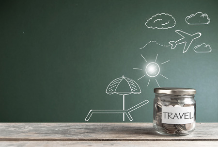 Travel savings jar by a chalkboard with vacation themed sketchesの写真素材
