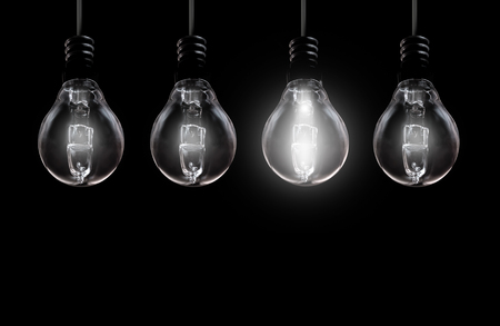 Brightly lit bulb on background with space in a row of unlit lampsの写真素材