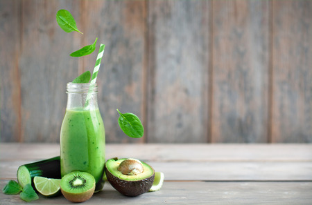 Fresh spinach leaves falling into a green smoothie on a wooden backgroundの写真素材