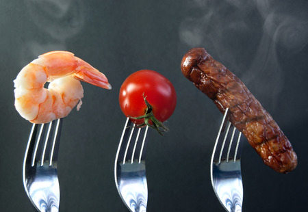 Barbecue ingredients including shrimp, tomato and sausage on forksの写真素材