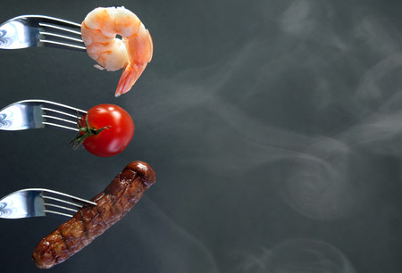 Barbecued ingredients including shrimp and sausage on forks with background spaceの写真素材
