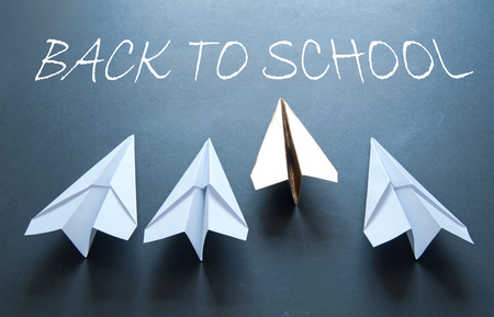 Back to school handwritten on chalkboard with gold paper plane standing out in a line of white planeの写真素材