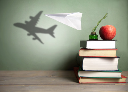 Success in education concept, paper plane with shadow of an aircraft next to a stack of books, quill and appleの写真素材