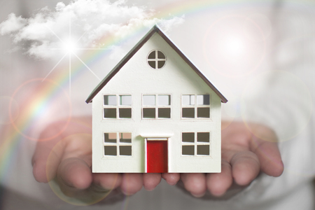 Small house in a hand with sun clouds and rainbow の写真素材