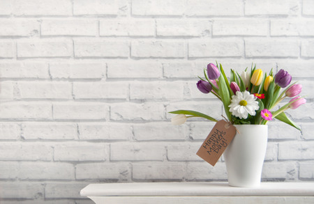 Mothers day spring flowers inside a pot on top of a fireplace mantelpiece with labelの写真素材