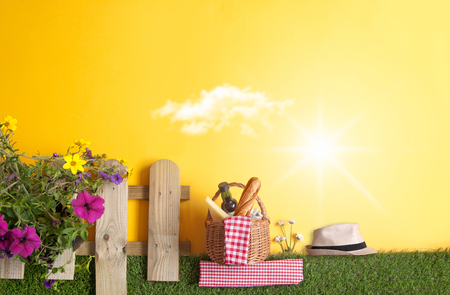 Summer picnic basket with bread, cheese and wine on grass with garden fence and flowersの写真素材