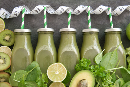 A row of green bottled smoothies with straws and fresh ingredients and a measuring tapeの写真素材