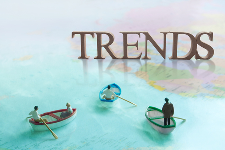 Miniature people sailing towards the word trends wooden blocks over a world mapの写真素材