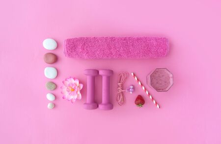Health and excercise accessories, including dumbbells, towel, and a berry smoothie with straw on a pink backgroundの写真素材