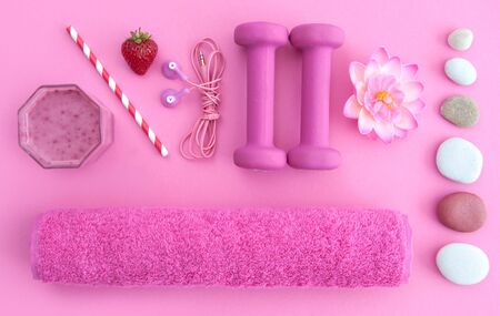 Health and excercise accessories, including dumbbells, towel, and a berry smoothie with straw on a pink backgroundの写真素材