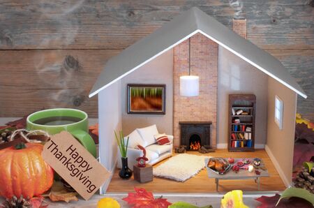 Happy thanksgiving label attached to miniature house living room and fireplace, with seasonal food laid out on a tableの写真素材