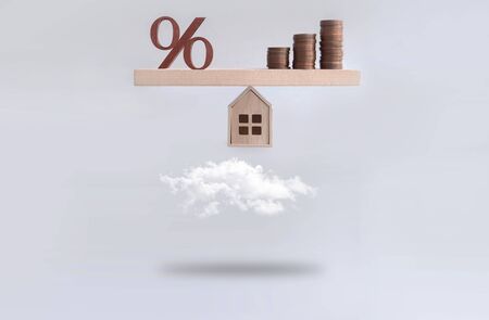 Percentage sign and stack of coins seasaw balanced on a miniature house hovering above the clouds, mortgage, investment conceptの写真素材