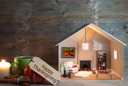 Happy thanksgiving label attached to miniature house living room and fireplace, as well as seasonal food laid out on a tableの写真素材