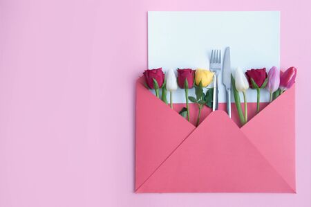 Envelope with assorted roses and tulips and knife and fork in the centre with blank sheet of paperの写真素材
