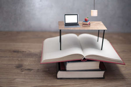 Miniature desk with laptop on top of open booksの写真素材