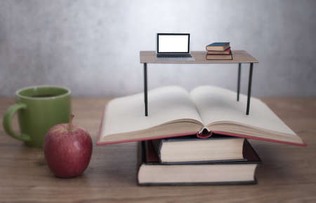 Miniature desk with laptop and books on an open stack of booksの写真素材