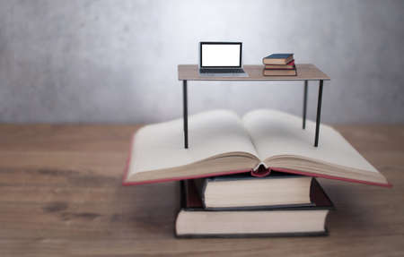 Miniature desk with laptop and books on an open stack of booksの写真素材