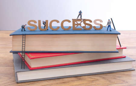 Miniature construction builders working around letters spelling success on top of a stack of booksの写真素材