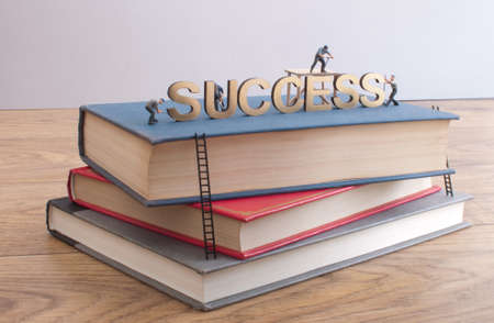 Miniature construction builders working around the golden heading succcess on top of a stack of booksの写真素材