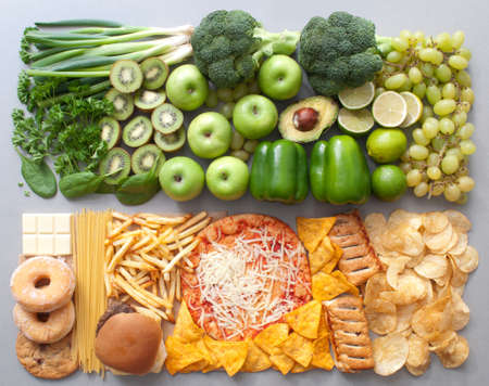Assorted group of green fruits and vegetables alongside beige junk foodの写真素材