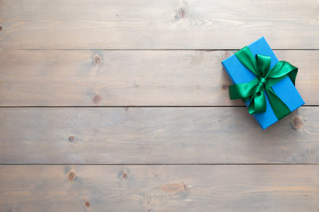 Blue gift box wrapped with green silk ribbon on a wooden table backgroundの写真素材