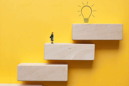 Miniature woman on steps looking towards light bulb aboveの写真素材