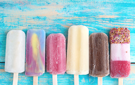 Assorted fruit and chocolate flavoured ice lolly sticks on wooden backgroundの写真素材