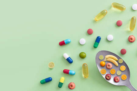 Spoon containing fruit including apples, bananas, lime and oranges alongside vitamin pills and...