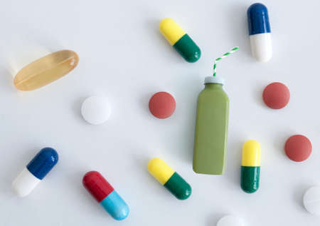 Green smoothie beverage standing out alongside many vitamin pillsの写真素材