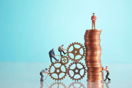 Miniature businessman on top of a pile of coins with construction workers, leadership, success conceptの写真素材