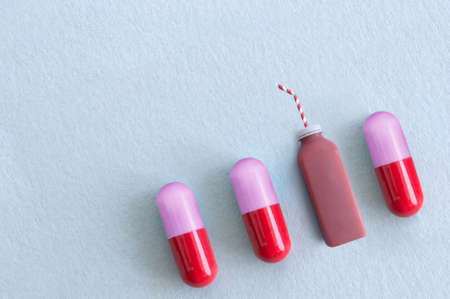 Fresh berry smoothie bottle with straw alongside vitamin pills