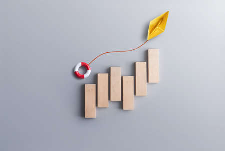 Financial success recovery concept, business chart wood blocks with paper boat carrying a life float buoy  moving upwardsの写真素材