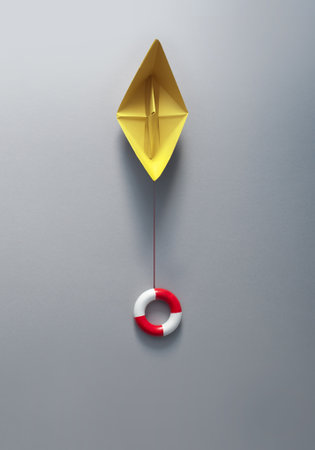 Buoy attached to paper boat symbolising business recovery, insurance, and rescueの写真素材