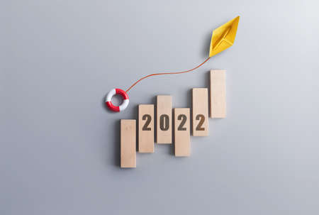 2022 financial success recovery concept, business chart wood blocks with paper boat carrying a life float buoy moving upwardsの写真素材