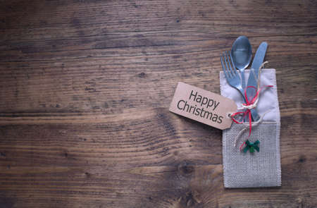 Christmas meal table setting, greeting card attached to fork and knife on wooden tableの写真素材