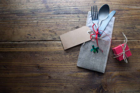 Festive meal table setting, greeting card attached to fork and knife on wooden tableの写真素材