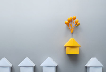 Orange paper house with balloons standing out amongst white housesの写真素材