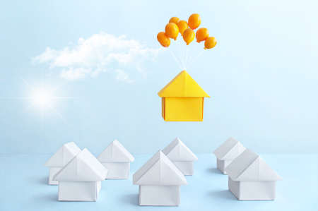 Orange paper house with balloons floating above many housesの写真素材