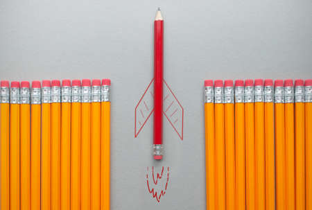 Red pencil with rocket sketch standing out amongst a row of orange pencilsの写真素材