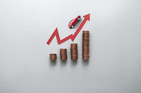 Increasing petrol price concept, business chart stacks of coins with toy car moving upwards along arrowの写真素材