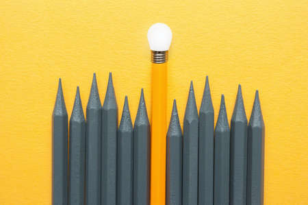 Orange pencil standing out amongst grey pencils with light bulb tip, unique ideas success conceptの写真素材
