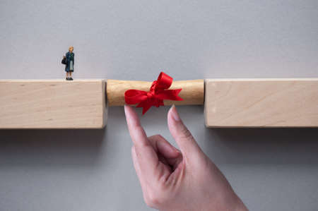 Graduation scroll bridging the gap between wooden blocks for female miniature figure to cross to the other sideの写真素材