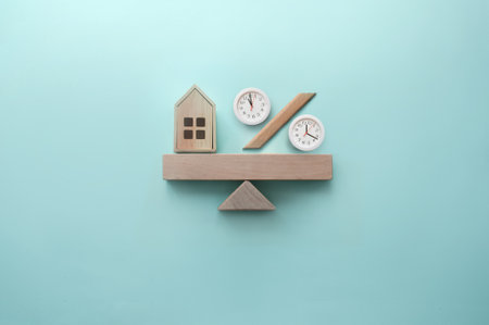 Miniature house and percentage sign with clocks balanced on a seesaw