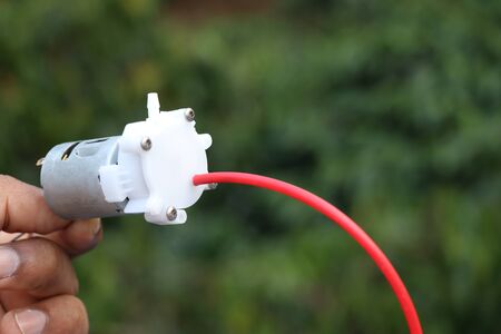 Small dc motor powered water pump with small tubes held in handの写真素材